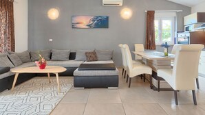 A modern living room with a grey sofa, a dining table with chairs, a coffee table, and a painting on the wall. - Vacation home Goldi by Interhome (Pula/Vodnjan)
