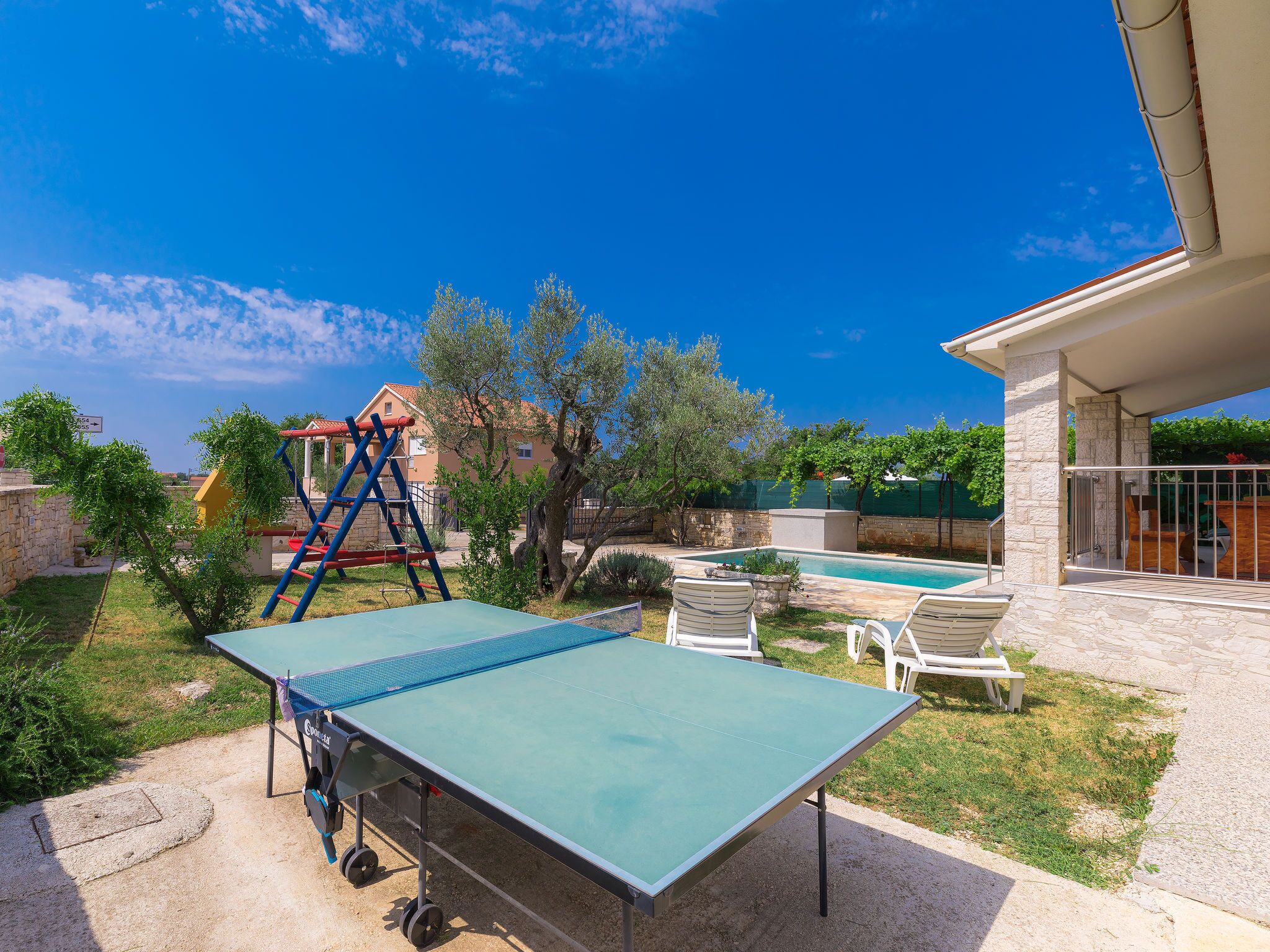 Ein Ping-Pong-Tisch in einem Hinterhof mit Pool, Sitzgelegenheiten im Freien und einer Kletterkonstruktion.