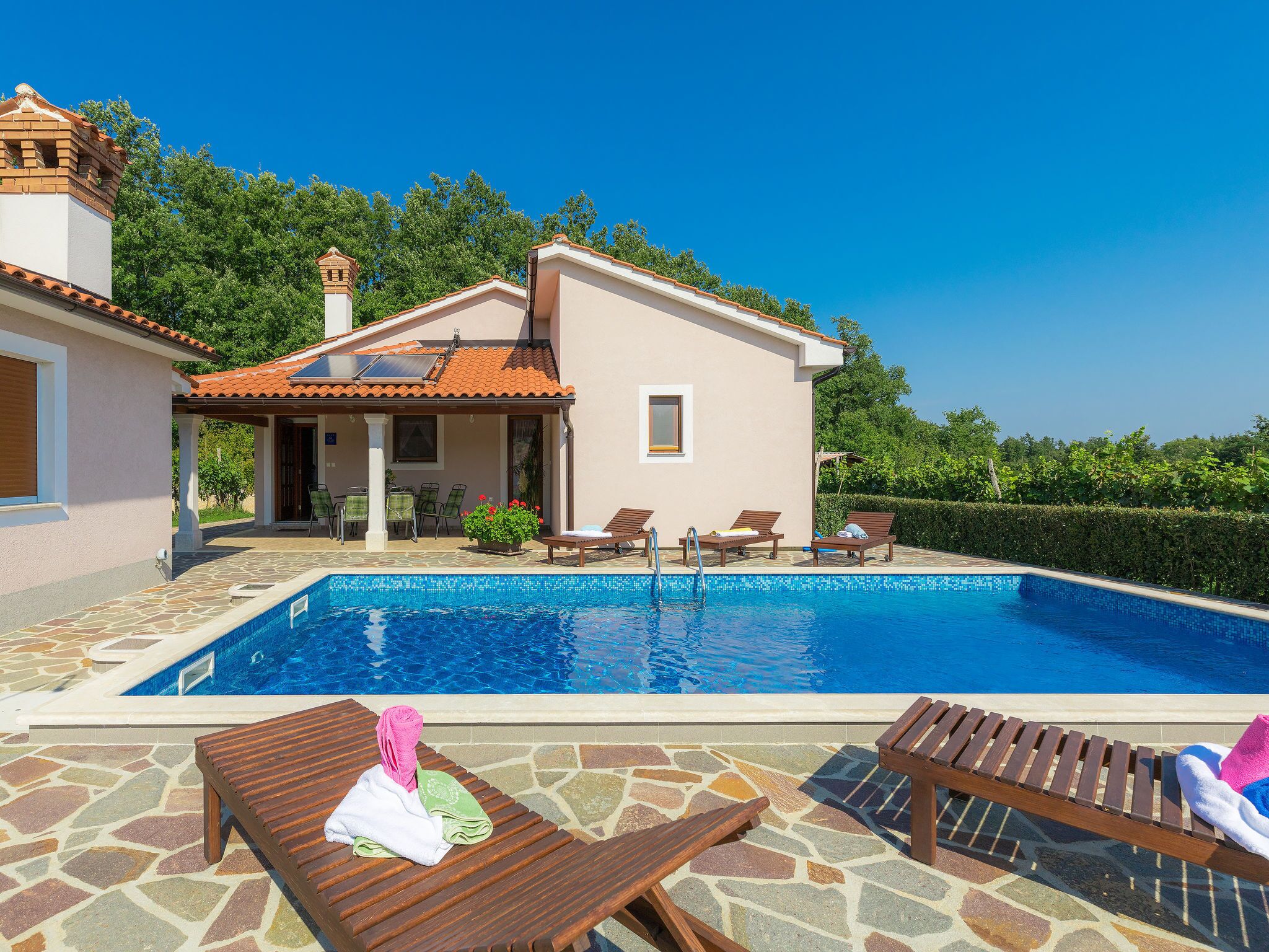 A poolside area with lounge chairs, a swimming pool, and a house with a tiled roof.