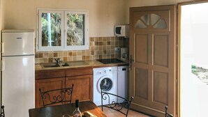 Une cuisine compacte équipée d’un réfrigérateur, d’un lave-linge et d’une fenêtre donnant sur un espace verdoyant.