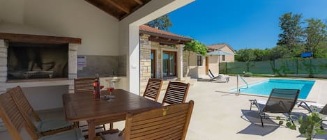Eine Außenpatio mit Pool, Holzmöbeln und einem Steinhaus im Hintergrund.