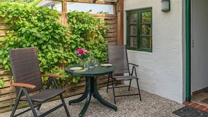 En terrasse med et rundt bord, to stole, et træhegn og et vindue.