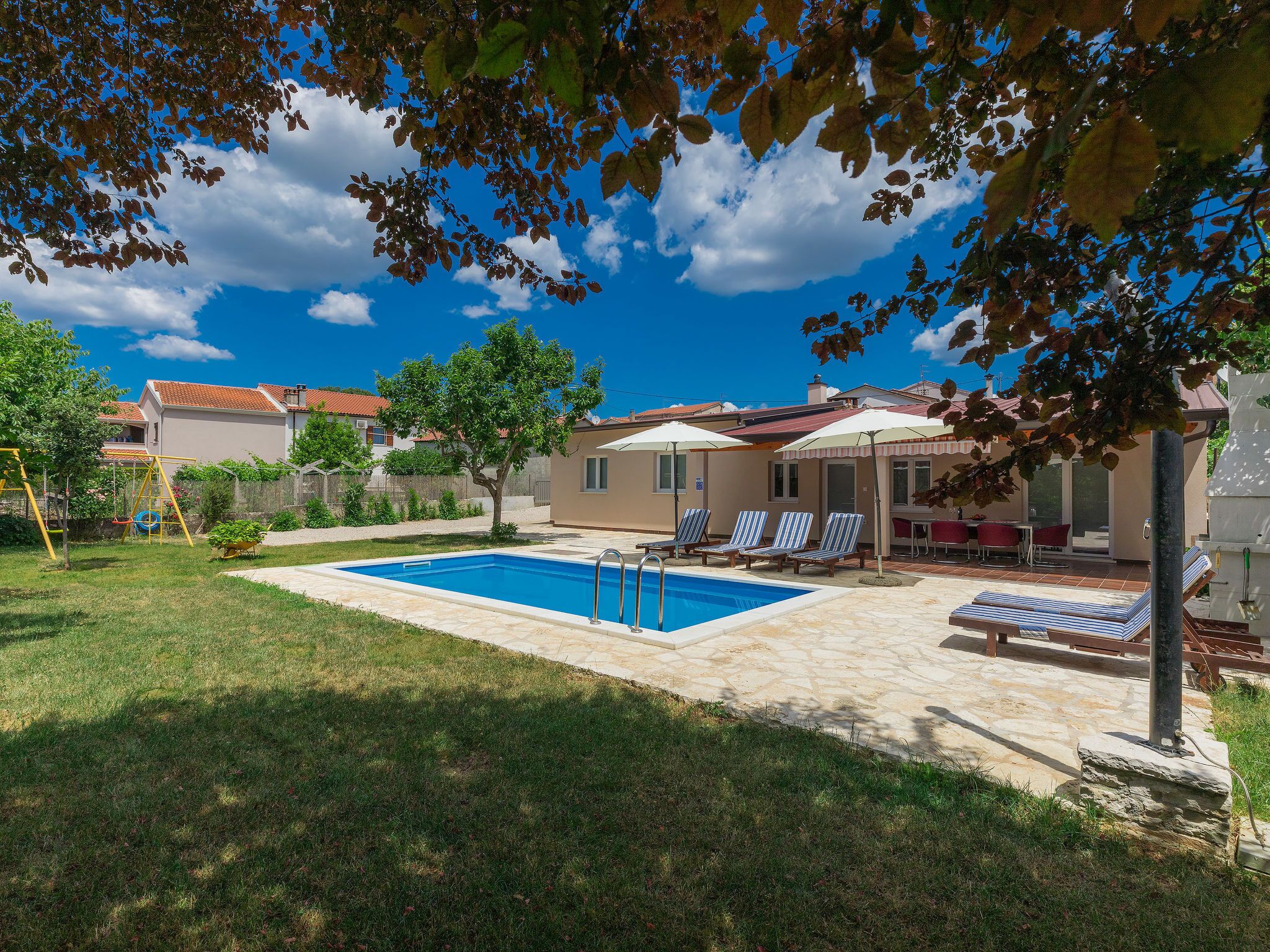 A swimming pool with lounge chairs and umbrellas, surrounded by a grassy area and trees.