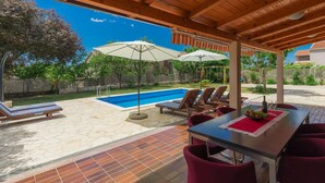 A covered outdoor area with a pool, lounge chairs, and a dining table with red chairs. - Vacation home Vrt by Interhome (Rovinj)