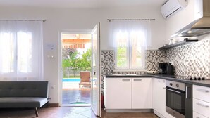 A modern kitchen with white cabinets, a black stove, and a tiled backsplash. - Vacation home Vrt by Interhome (Rovinj)
