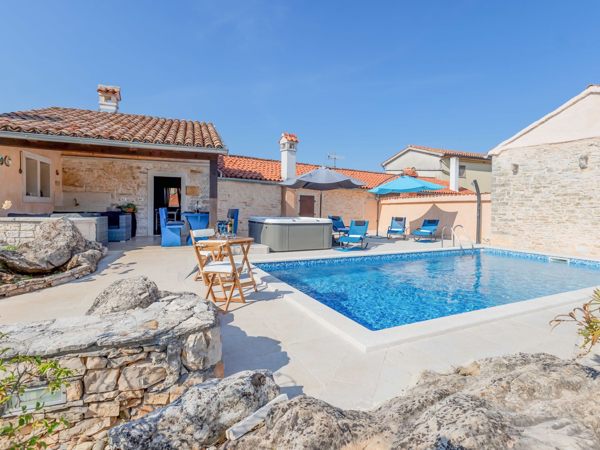 A swimming pool area with lounge chairs, a hot tub, and stone walls.