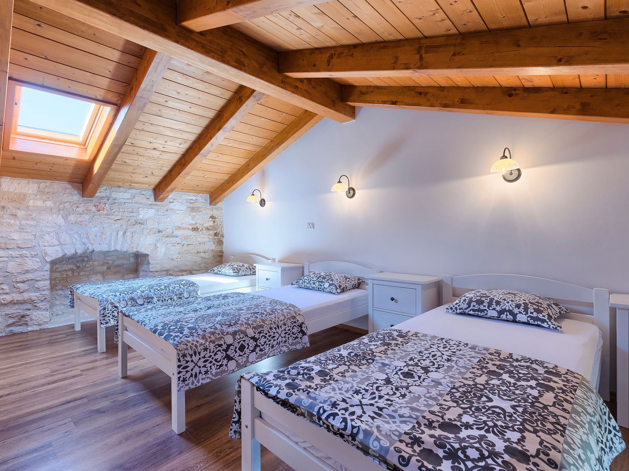 A cozy bedroom with two beds, wooden beams, stone walls, and a skylight.