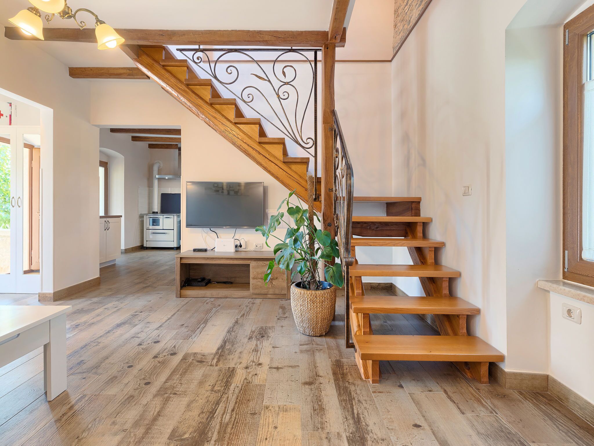 A spacious living area with a wooden staircase, a flat-screen TV, and a potted plant.