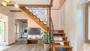 A spacious living area with a wooden staircase, a flat-screen TV, and a potted plant.