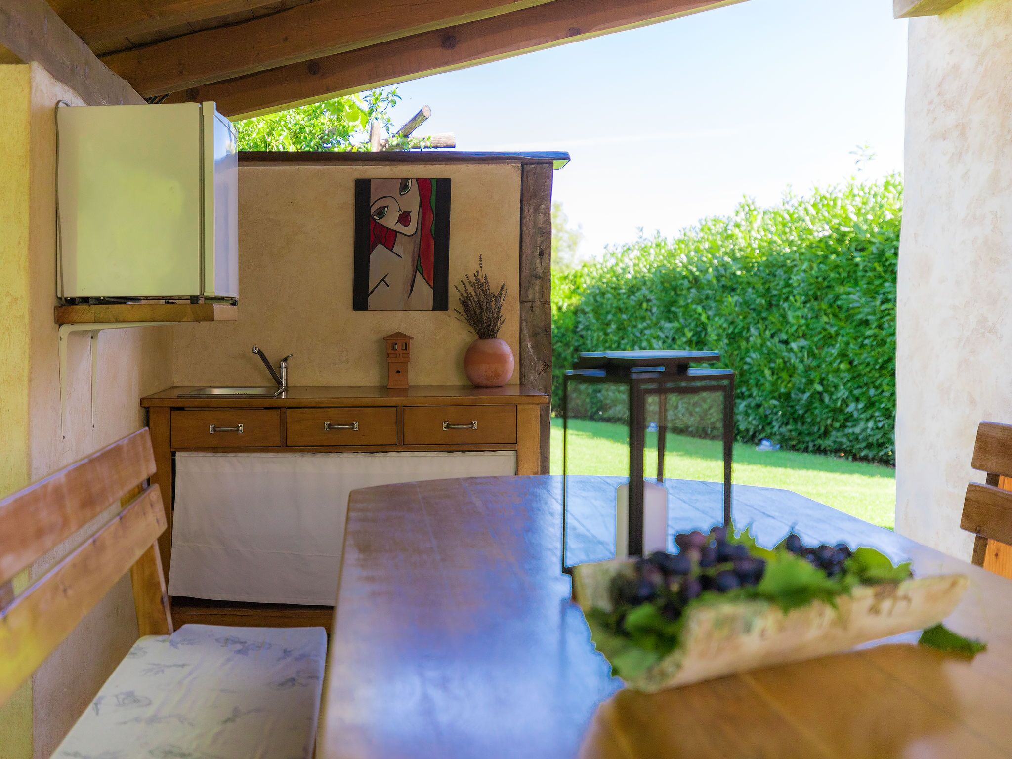A kitchen with a wooden countertop, a sink, and a small cabinet. There is a painting on the wall and a potted plant on the counter.