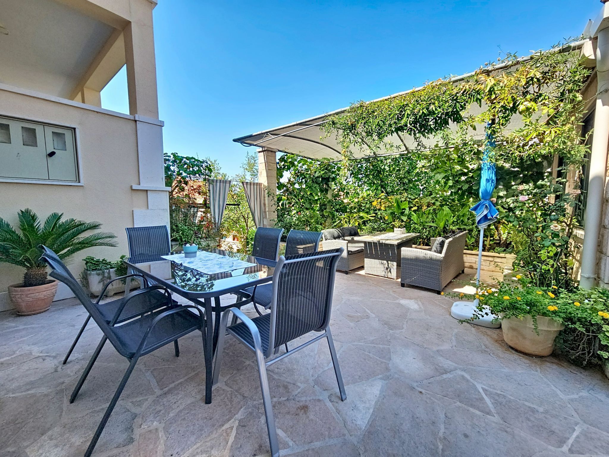 An outdoor patio with a table and chairs, surrounded by potted plants and a covered seating area.
