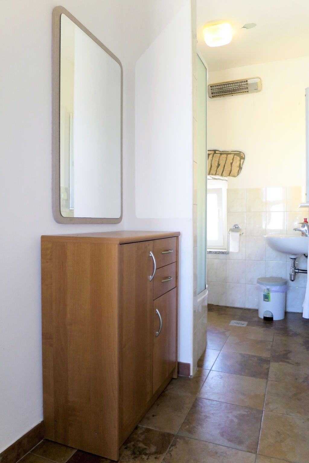 A bathroom with a wooden cabinet, a mirror, a sink, and a toilet.