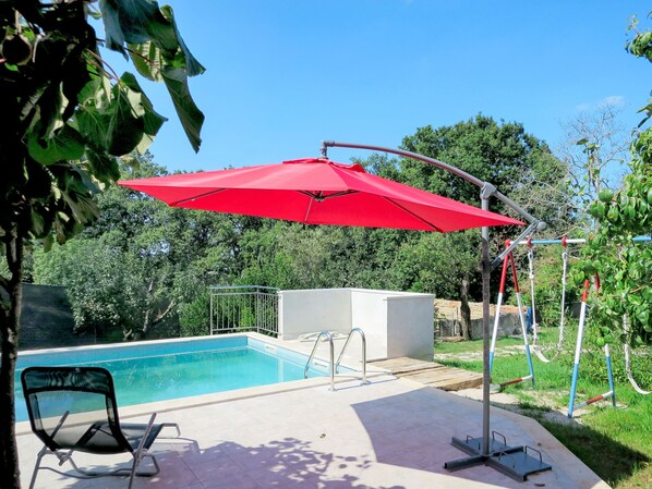 A swimming pool with a red umbrella, a small deck, and a chair.