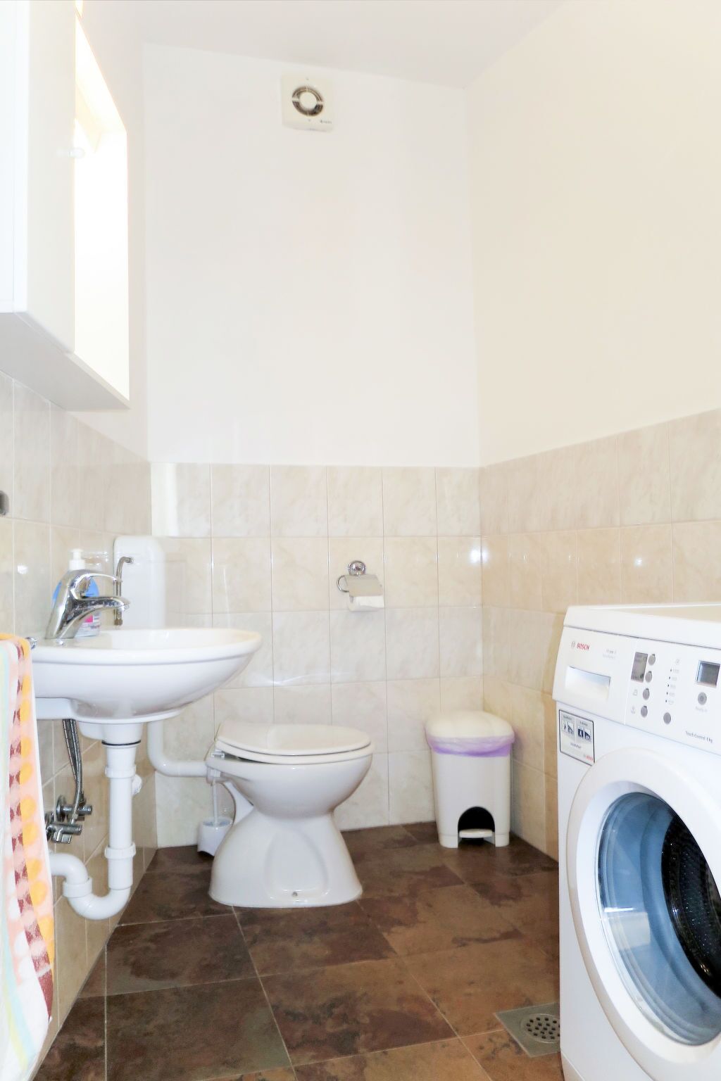 A compact bathroom with a sink, toilet, bidet, and a washing machine.