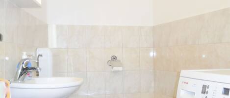 A compact bathroom with a sink, toilet, bidet, and a washing machine.
