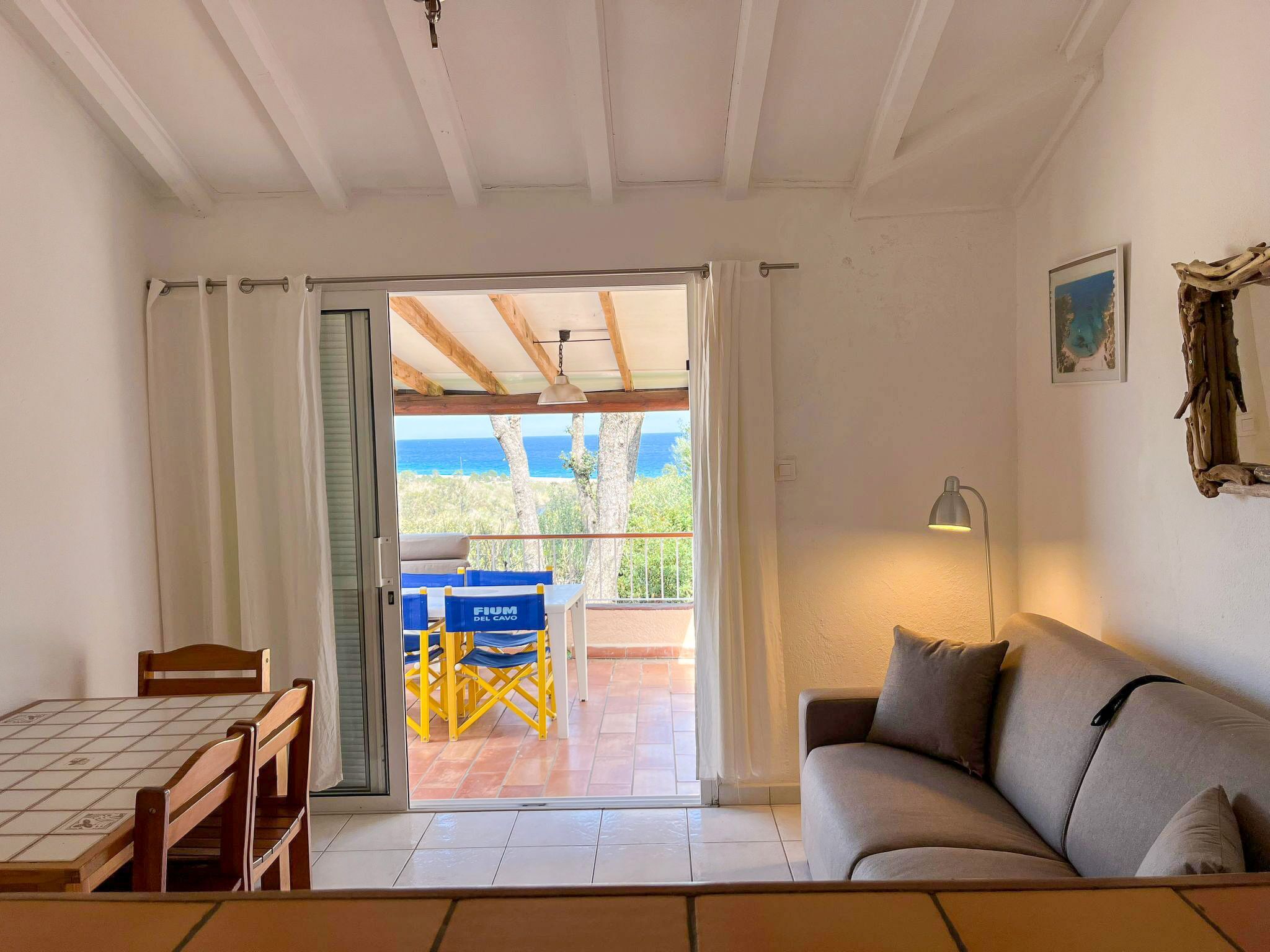 A room with a balcony, a sofa, a table with chairs, and a view of the ocean.