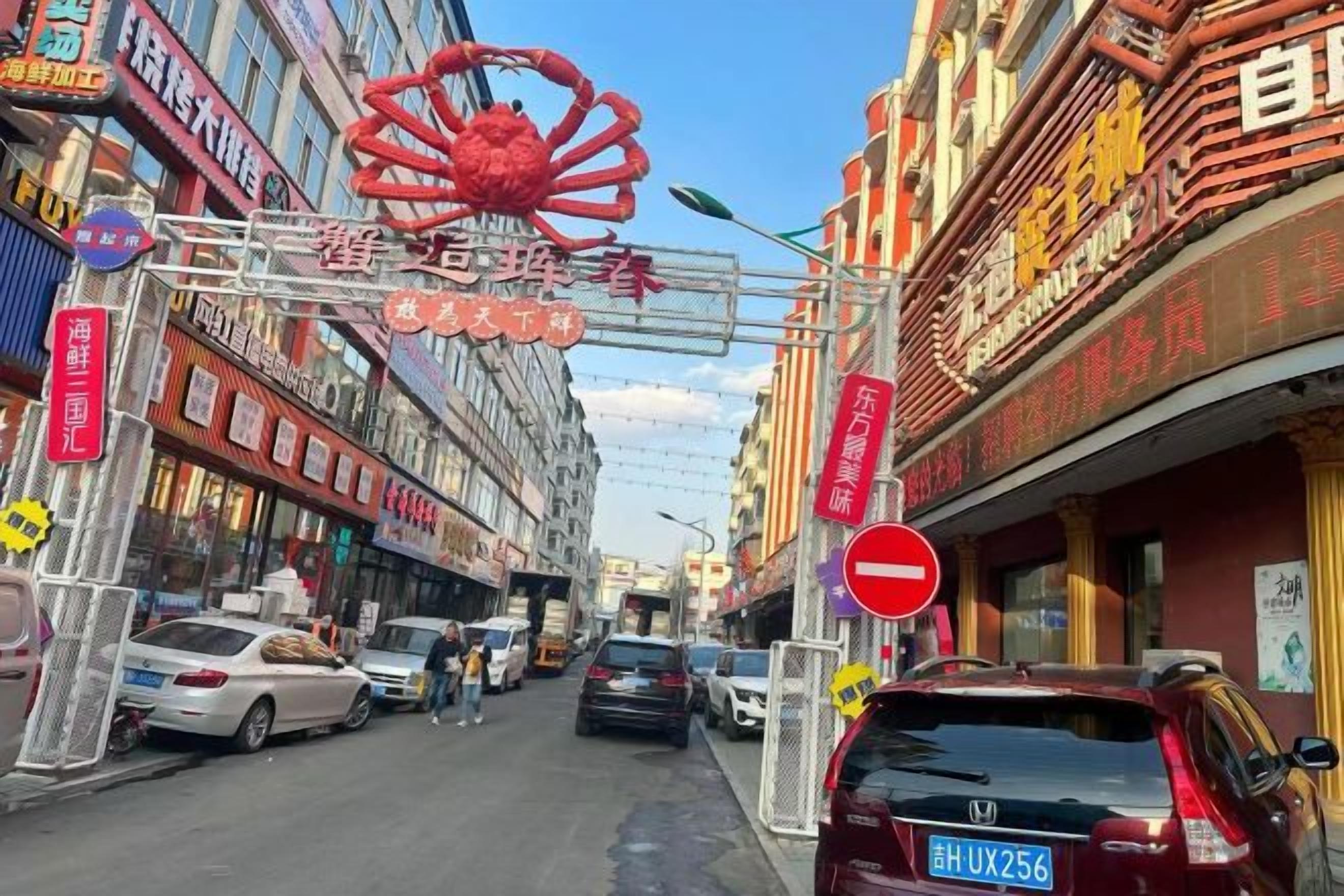 Una strada con auto parcheggiate lungo il lato, edifici con insegne e una grande decorazione a forma di granchio rosso.