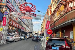 A street with cars parked on the side, buildings with signs, and a large red crab decoration. - Wudi Business Hotel (Hunchun)