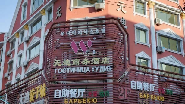 A building with multiple signs, including one for a hotel named "Gostinitsa Udi" and another for a self-service restaurant named "Barbeko". - Wudi Business Hotel (Hunchun)