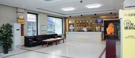 Un vestíbulo de hotel con mostrador de recepción, zona de estar y una planta grande.