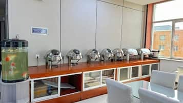 Een kamer met een lange balie, meerdere koffieautomaten voor zelfbediening, een aquarium en uitzicht op een gebouw door een raam.