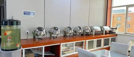 A room with a long counter, multiple self-service coffee machines, a fish tank, and a view of a building through a window.