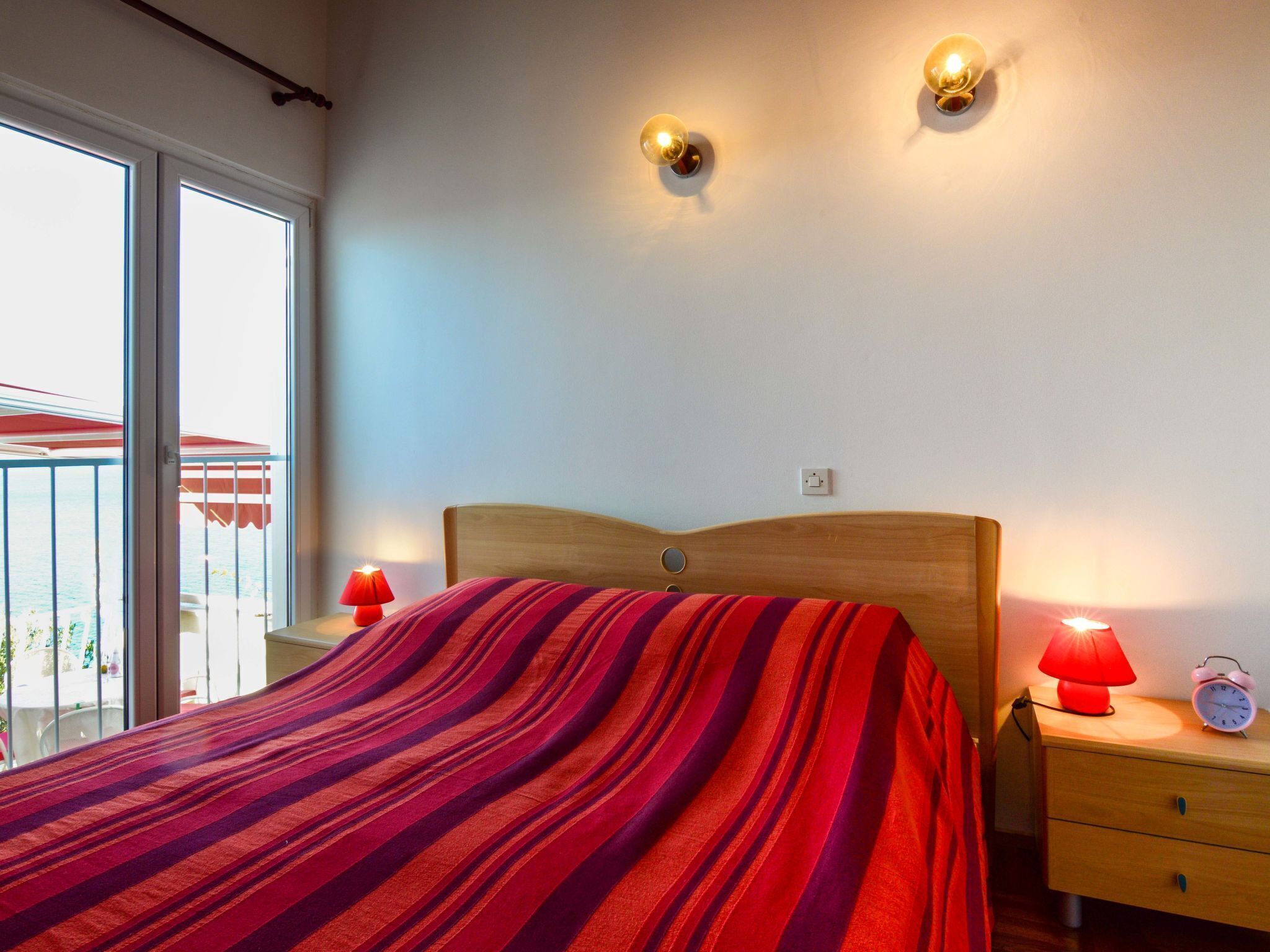 A bedroom with a bed, two bedside lamps, a nightstand, and a wall socket.