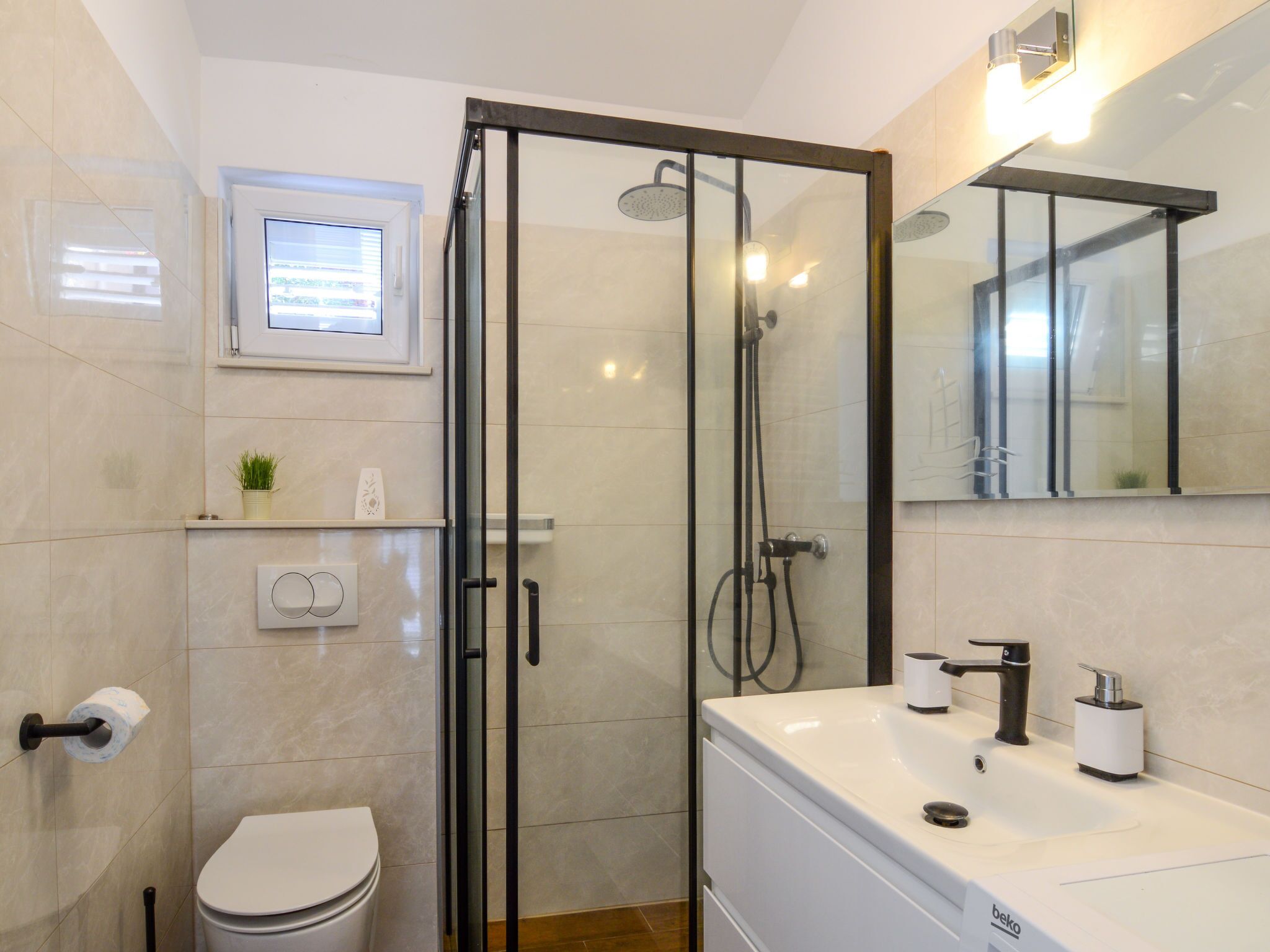 A modern bathroom with a glass-enclosed shower, a toilet, a sink with a mirror, and a small window above the toilet.