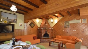 A cozy dining area with a brick fireplace, wooden ceiling beams, and orange furniture.