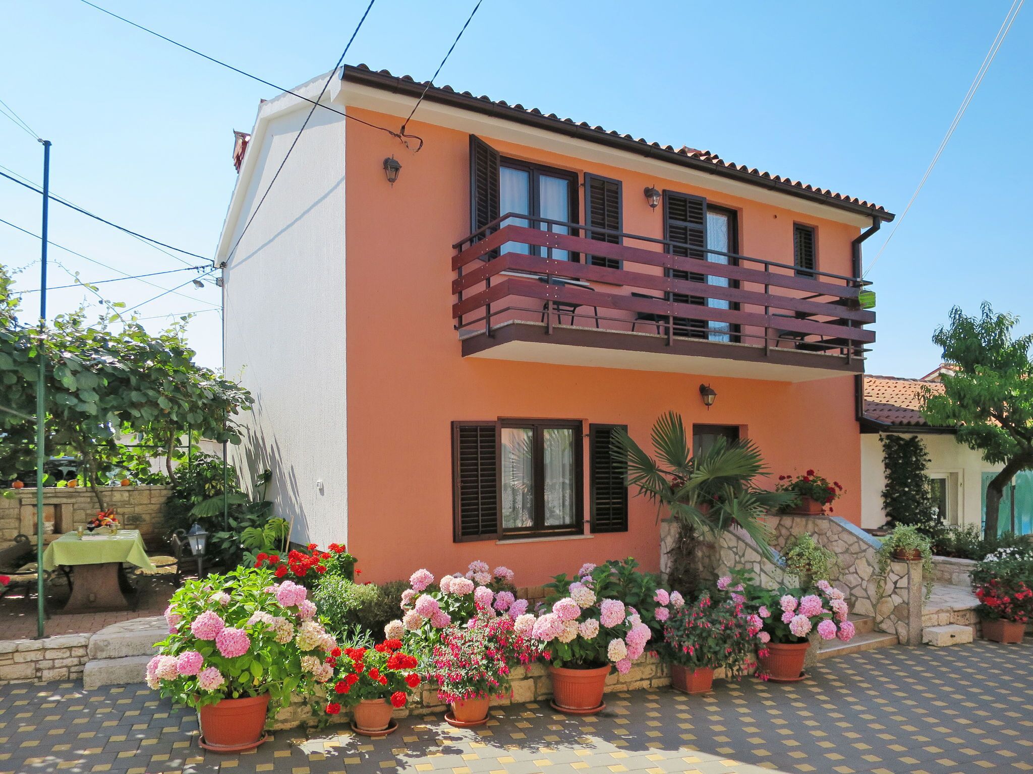 A two-story house with a balcony, potted plants, and a paved driveway.