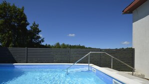 A swimming pool with clear blue water, surrounded by a concrete deck and a wooden fence.
