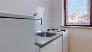 A kitchen with white cabinets, a stainless steel sink, a gas stove, and a window with a view of buildings. - Apartment Alba by Interhome (Rovinj)