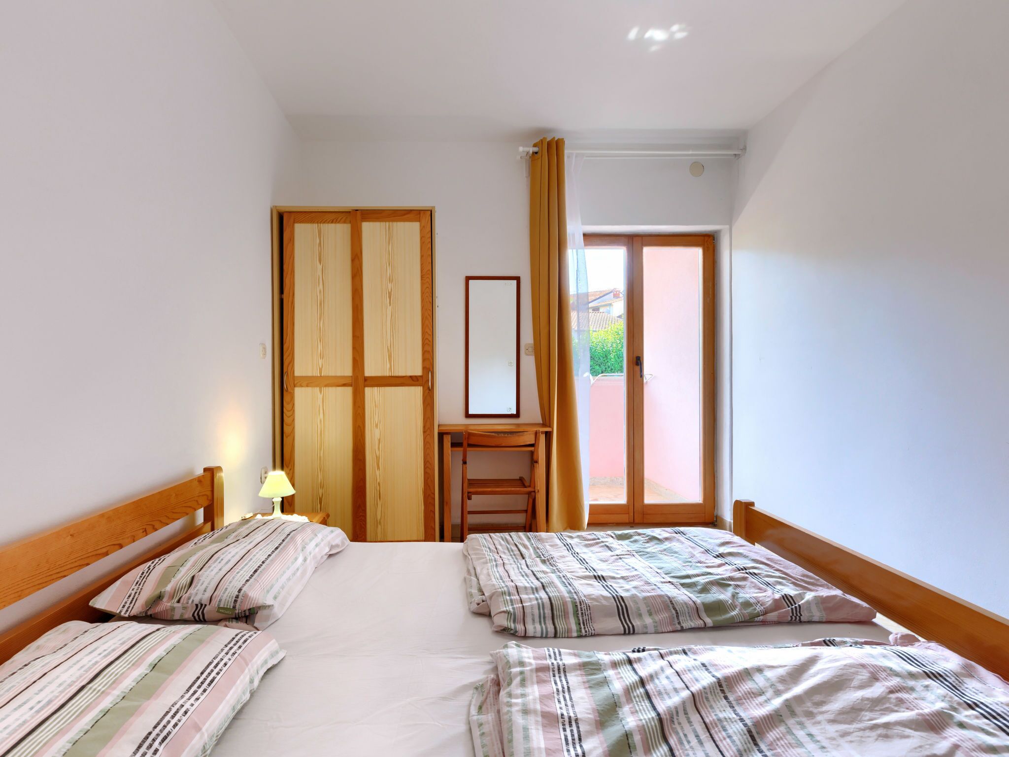 Ein Schlafzimmer mit zwei Betten, einem Holzschrank, einem kleinen Tisch und einer Glastür, die auf einen Balkon führt.
