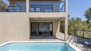 A modern two-story building with a swimming pool, large windows, and a balcony.