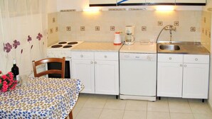 Cocina compacta con muebles blancos, estufa, cafetera y lavabo.