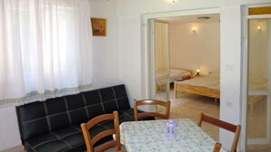 Ett mysigt rum med en svart soffa, trästolar, ett litet bord med ett blommigt bordsduk och en säng i bakgrunden.