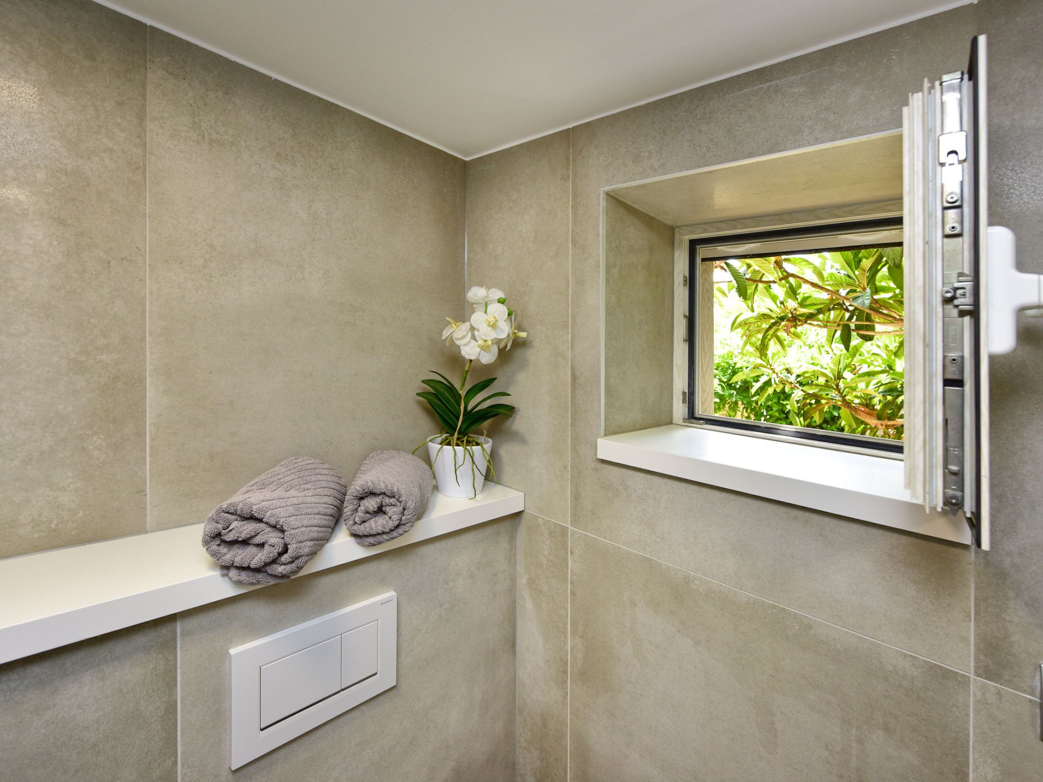 Ein Badezimmer mit Fenster, Handtuchhalter, Topfpflanze und Thermostat.