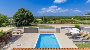 Una piscina con sillones de descanso y una pérgola, rodeada por un jardín ajardinado y vistas al campo.