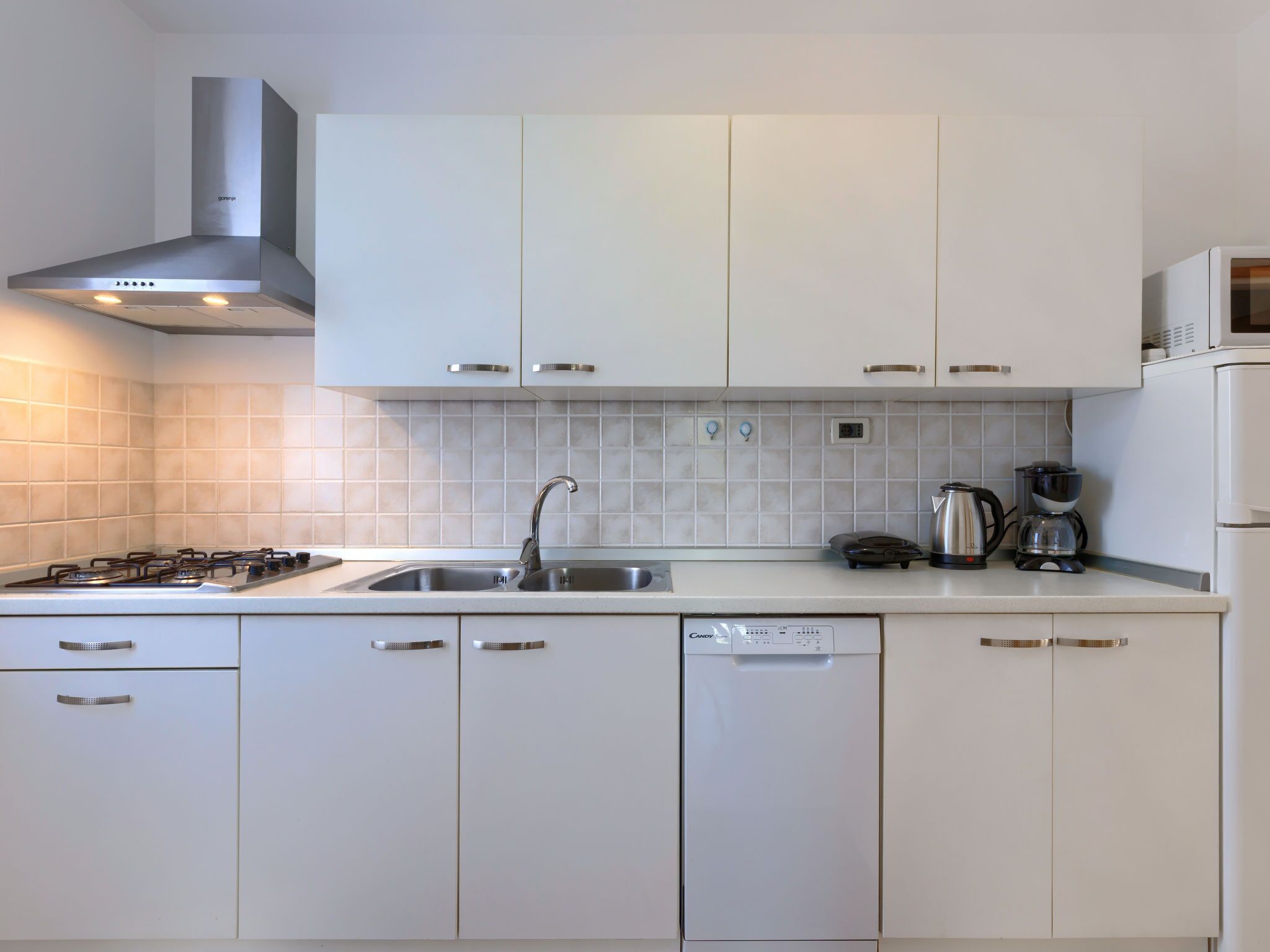 Una cocina moderna con armarios blancos, una campana extractora de acero inoxidable, un fregadero, lavavajillas y una cafetera.