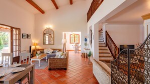 A spacious living area with a high ceiling, wooden beams, a staircase with ornate railings, and a dining area set up with a table and chairs. - Ponderosa by Interhome (Théoule sur mer)