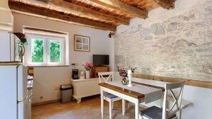 A cozy kitchen with a wooden ceiling, a stone wall, a window with greenery outside, a TV, and a dining area with a table and chairs. - Pinia I+II by Interhome (Poreč/Kaštelir)