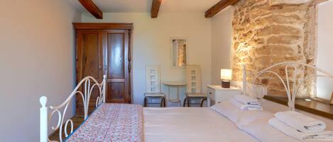 A bedroom with a large bed, a wooden door, a small table, and a stone wall.