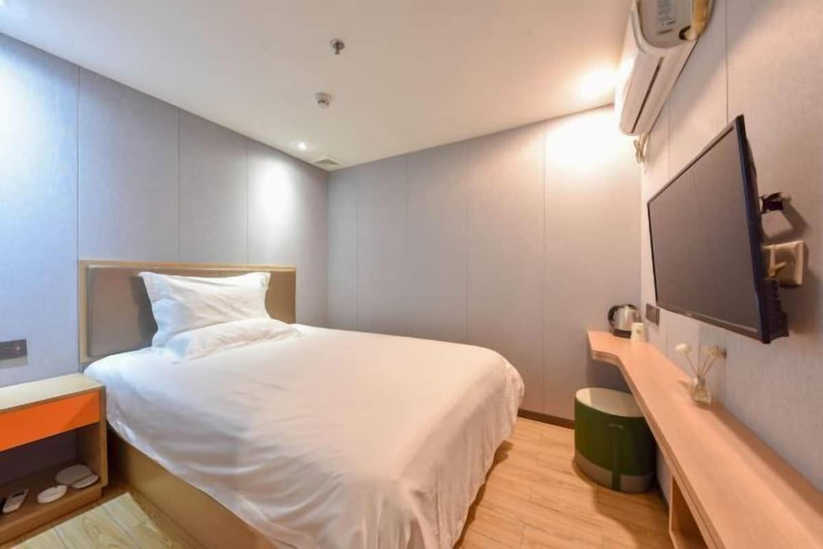 A modern hotel room with a bed, a TV mounted on the wall, a small table, and a trash bin.