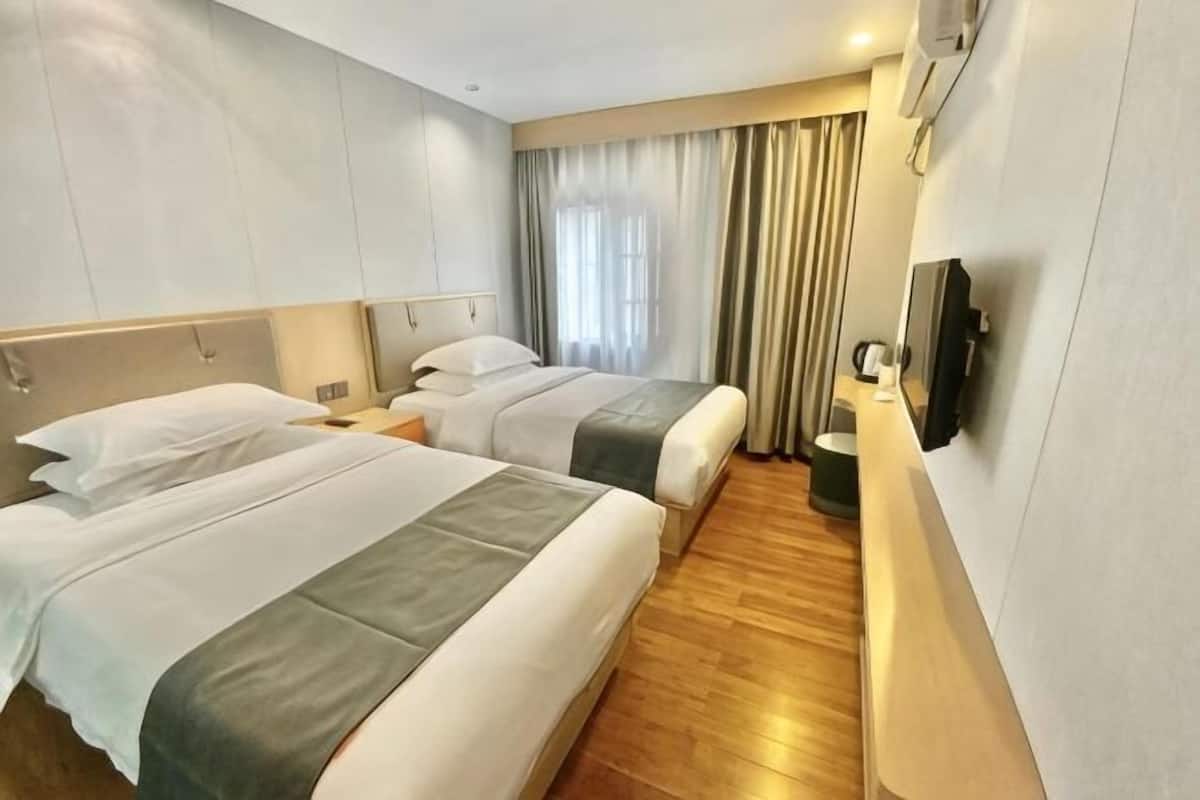 A hotel room with two beds, a TV, a bedside table, and a window with curtains.