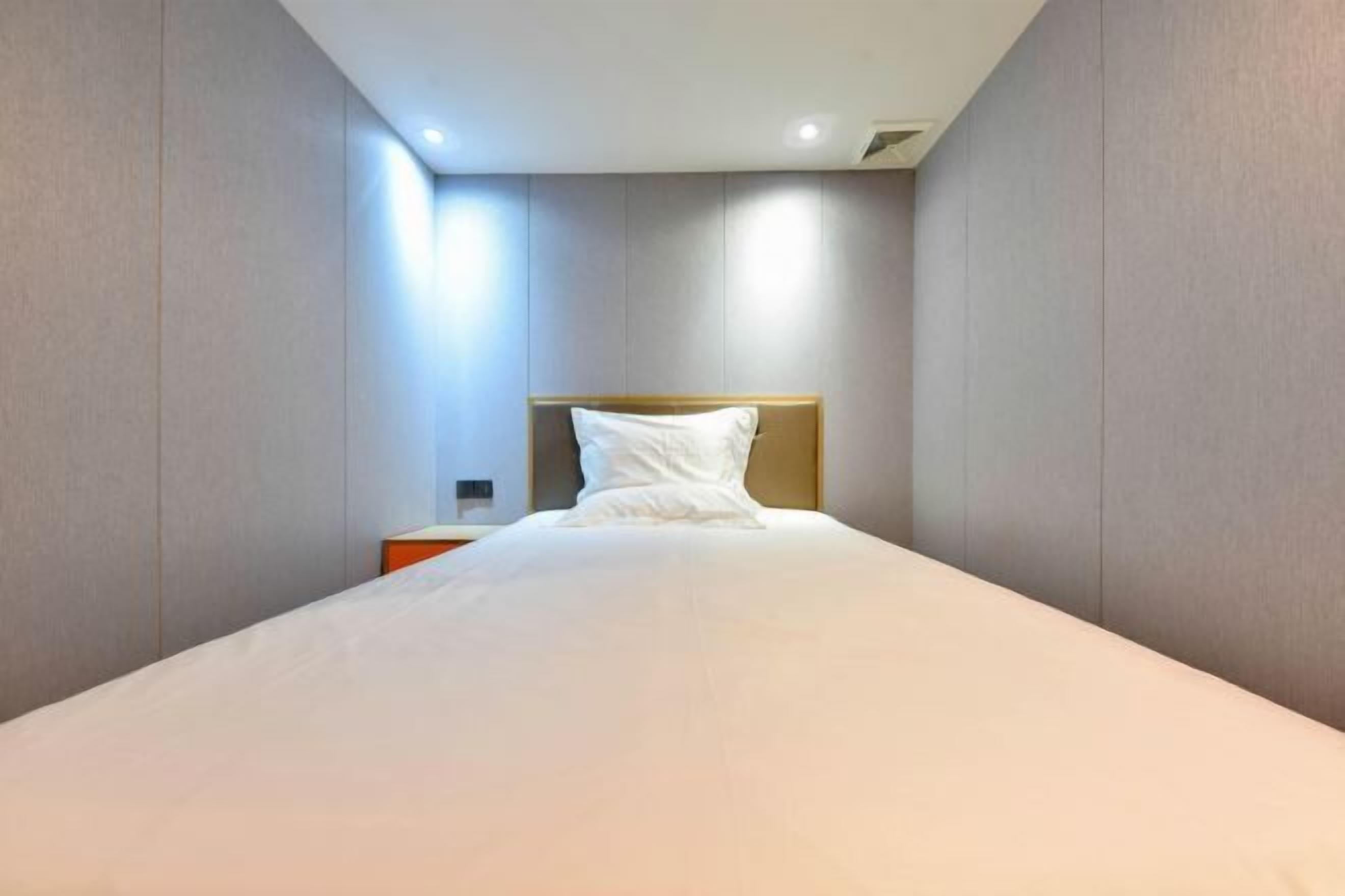 A modern hotel room with a large bed, a wooden headboard, and a nightstand with a lamp.