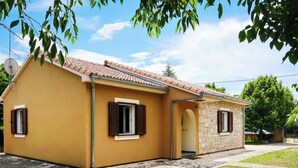 A yellow building with a tiled roof, a stone wall, and a small garden area. - Vacation home Ana by Interhome (Šibenik)