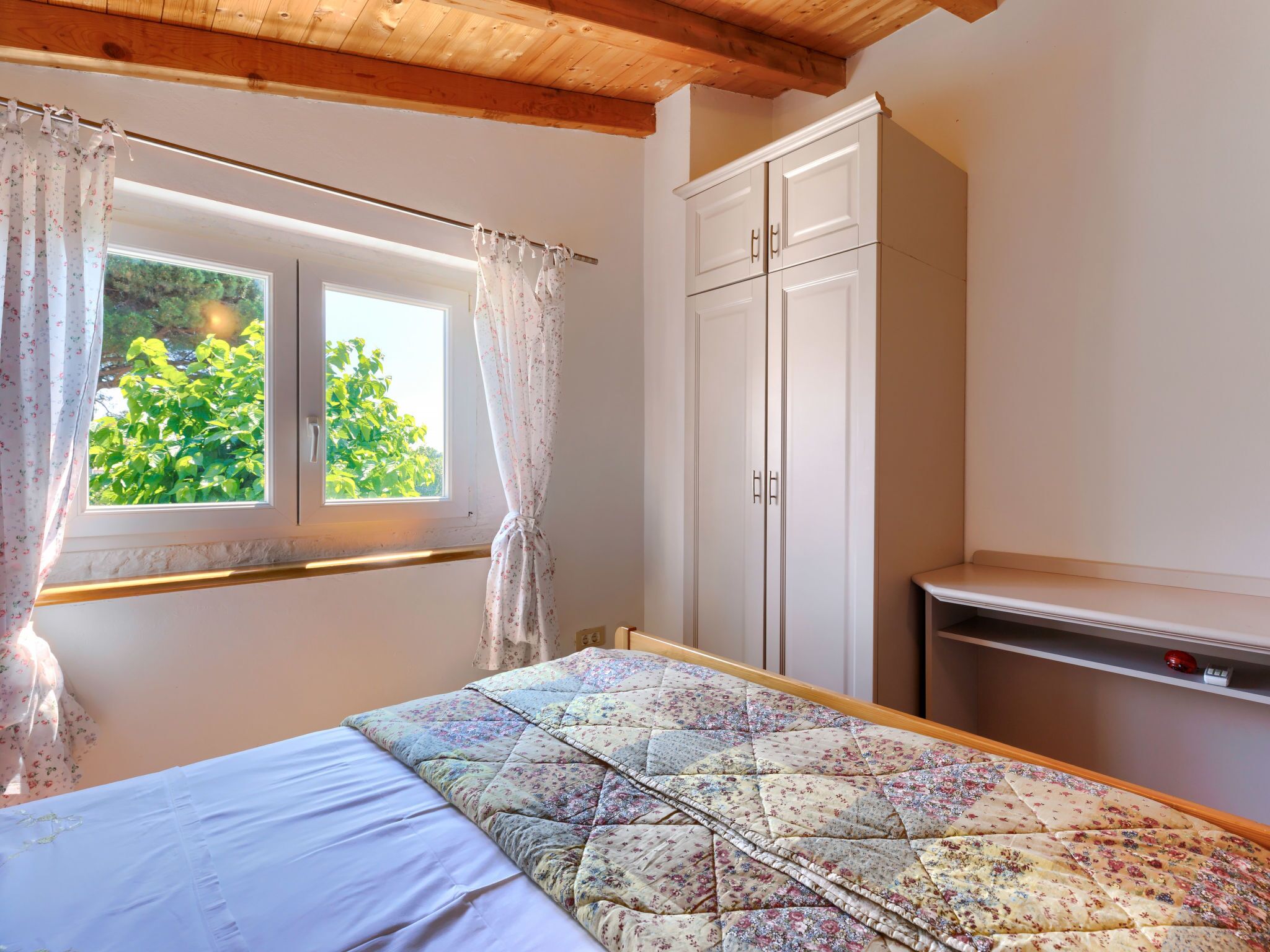 A bedroom with a bed, a window with curtains, a wardrobe, and a small shelf.