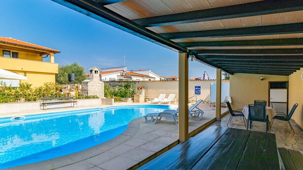 A covered swimming pool area with lounge chairs and a table, surrounded by buildings. - Apartment Dika by Interhome (Poreč)