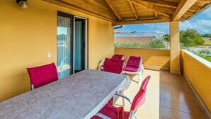 A covered outdoor area with a table and chairs, a sliding glass door, and a view of a building and greenery. - Apartment Dika by Interhome (Poreč)