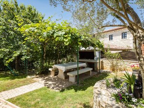 Relax in a serene outdoor space surrounded by lush greenery and flowering plants, complete with a grill for outdoor cooking.